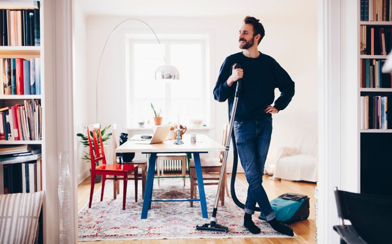 Happy man standing with vacuum cleaner in dining room at home
