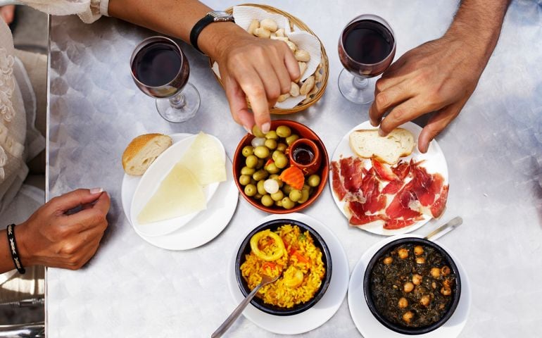 People eating tapas at outdoor restaurant, close-up of hands, overhead view