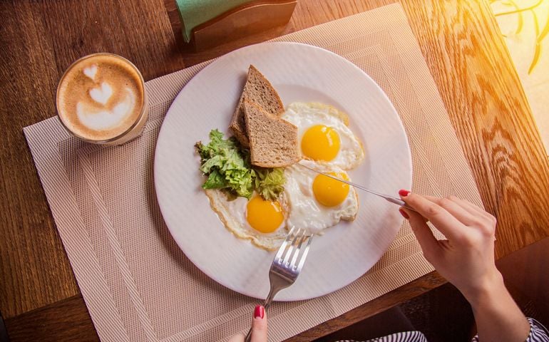 Woman eating fried eggs with toasts and coffee