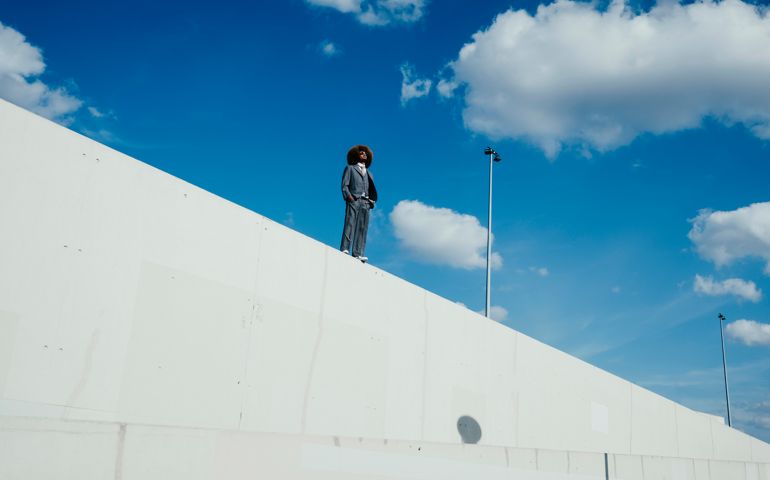 Cool, well-dressed young man with afro standing on sunny urban wall