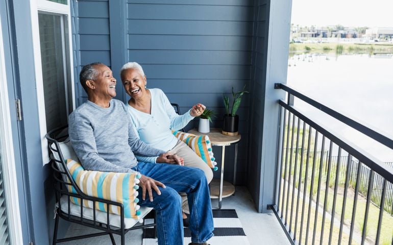 Senior couple relaxing on porch, holding hand, laughing
