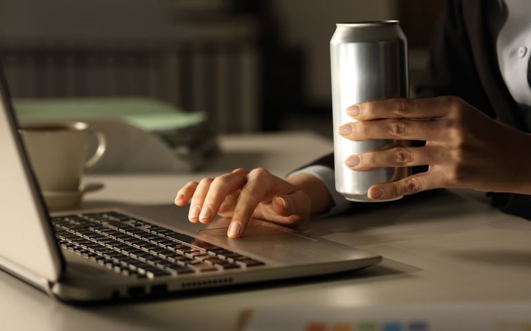 Close up of executive woman hands with laptop holding energy drink can at night in the office