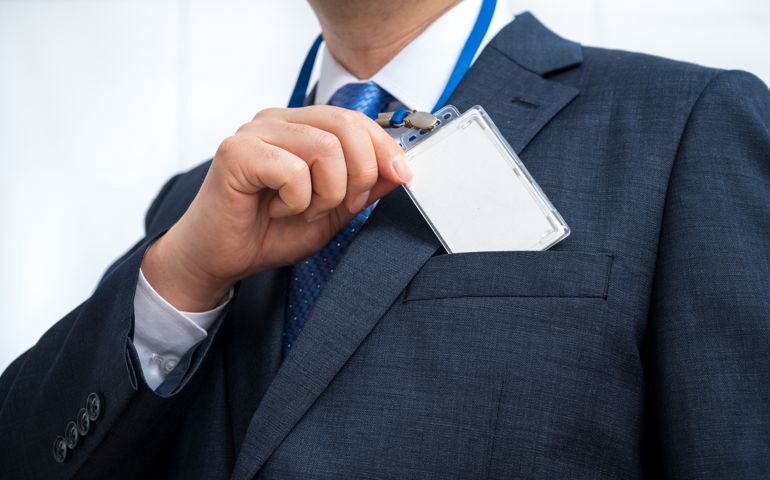 Businessman in suit wearing a blank ID tag or name card on a lanyard at an exhibition or conference.