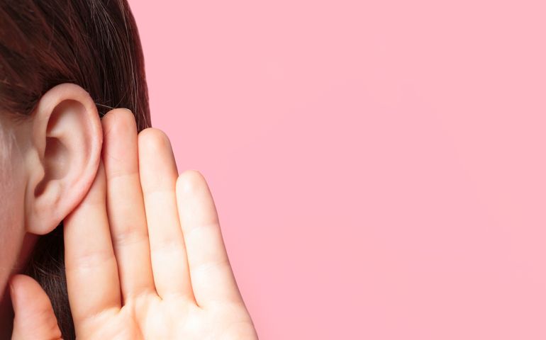 The girl listens attentively with her palm to her ear close-up on pink background
