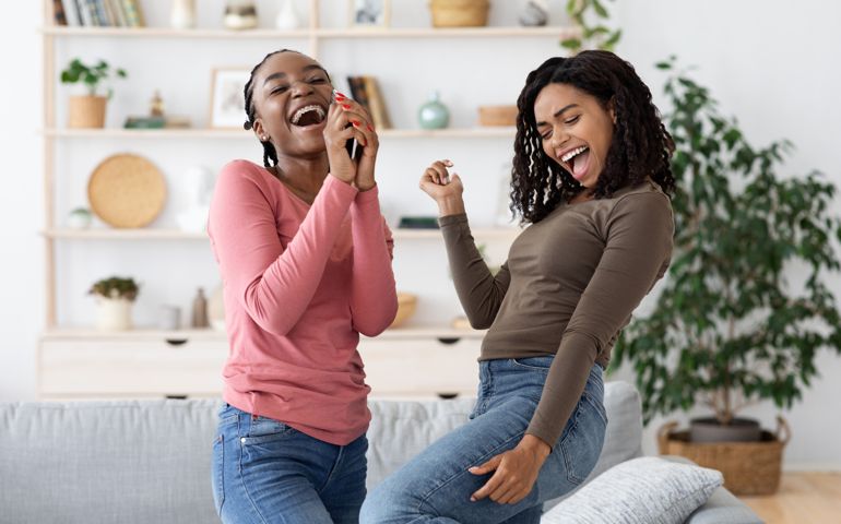 Carefree african american girlfriends singing and dancing at home