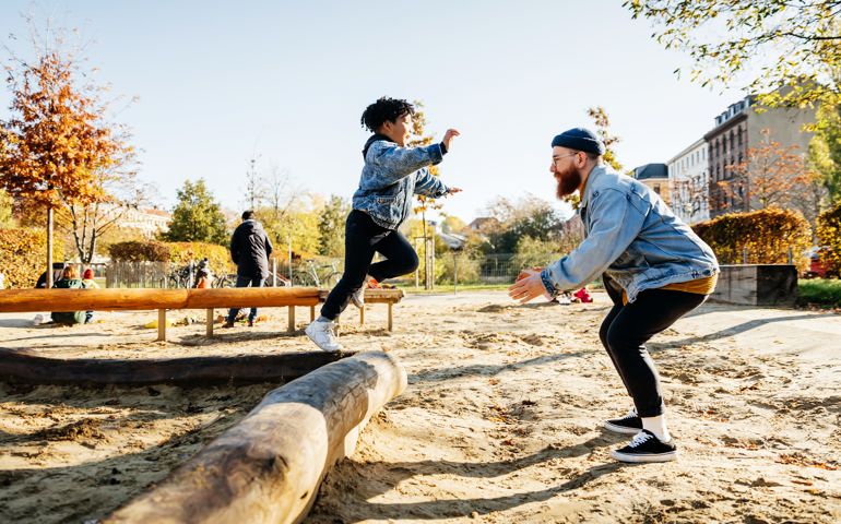 Young Boy Leaping Into Father Arms In Playground