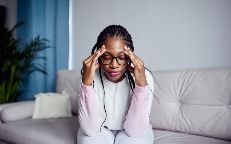 A young girl is sitting on the couch at home with her head in her hands.