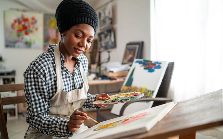 Afro female fine artist with traditional african hat and apron, drawing in art studio