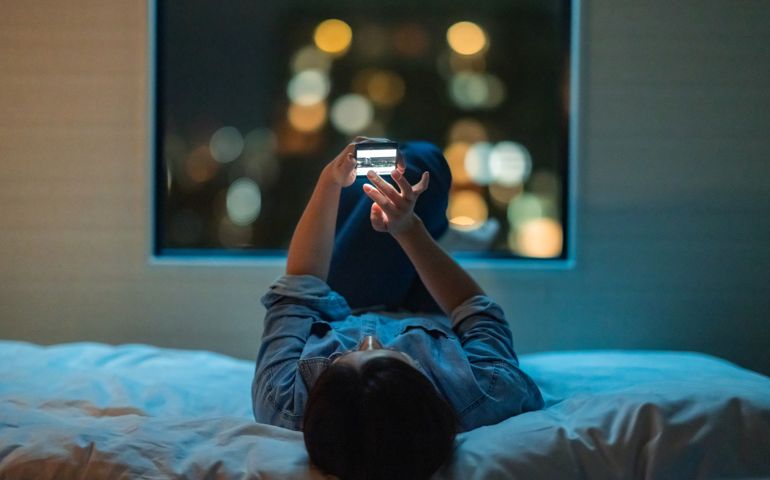 Woman lying down on bed and using smart phone at night