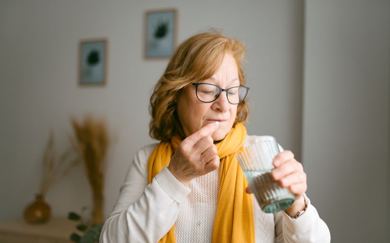 Portrait of a mature woman taking pills and vitamins standing by the living room window. With copy space to the left.