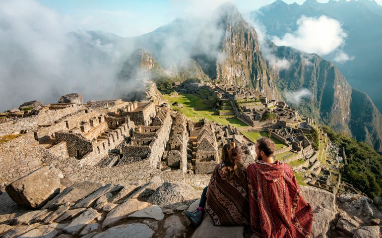 Couple dressed in ponchos watching the ruins of Machu Picchu, Peru