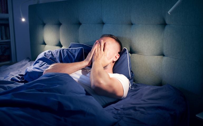 Frustrated man fighting with sleeping disorder. Holding head in hands