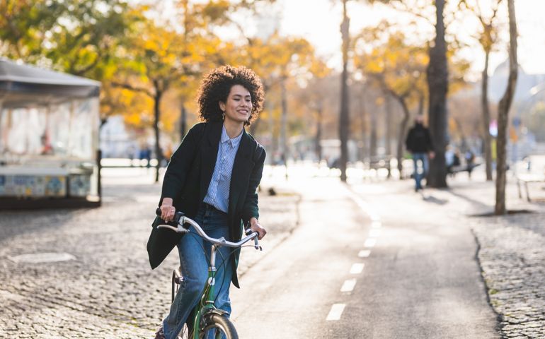 Beautiful woman with modern and relaxed look riding bike through park in autumn.