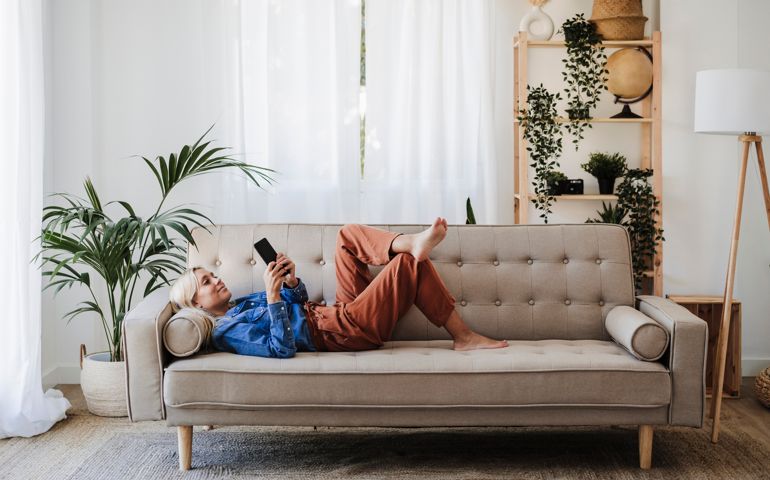 Young woman using mobile phone lying on sofa at home
