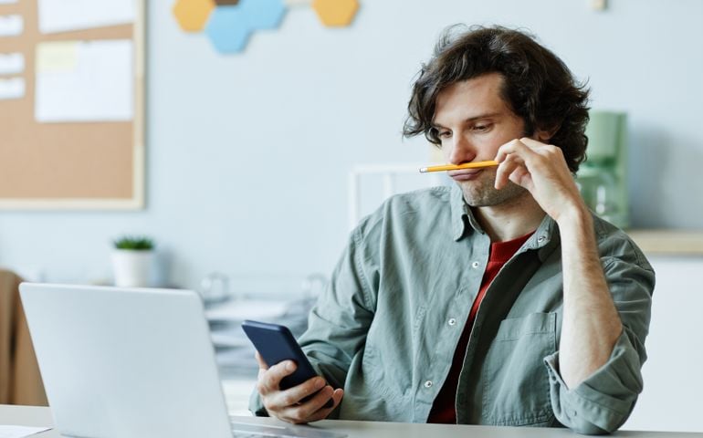 Bored Young Man in Office Using Phone