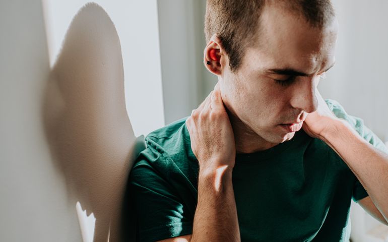 Conceptual image of a man holding his neck, either in physical or emotional pain