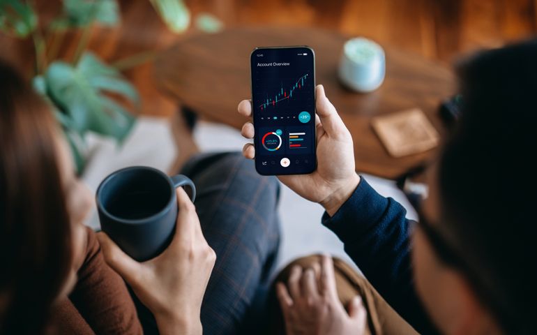 Young Asian couple managing finance and investment online, analyzing stock market trades with mobile app on smartphone. Making financial plans. Banking and finance, investment, financial trading, mobile banking concept