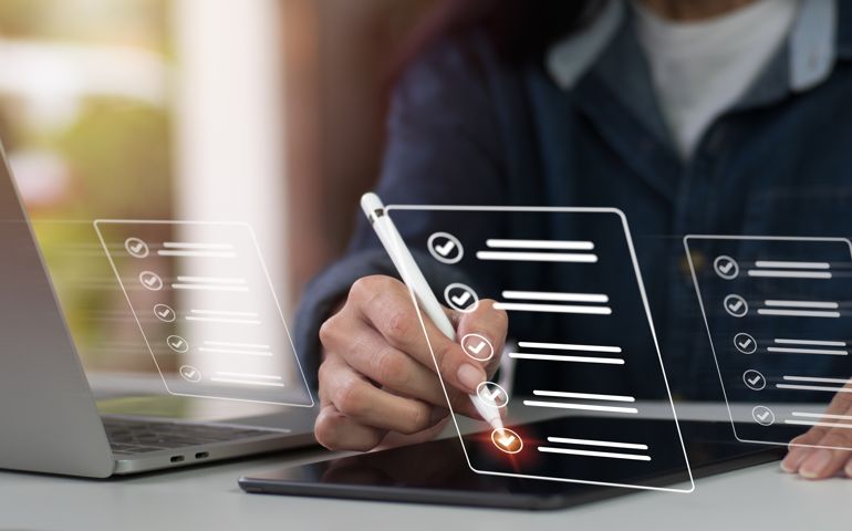 Concept of a company performance checklist, with a businesswoman completing a digital form checklist while using a laptop and tablet.
