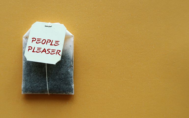 Teabag on yellow copy space background with text PEOPLE PLEASER, concept of one who tries hard to make others happy even go out of their way, time or resources,overly concerned with pleasing others