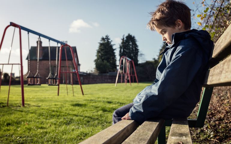 Lonely child sitting on play park playground bench