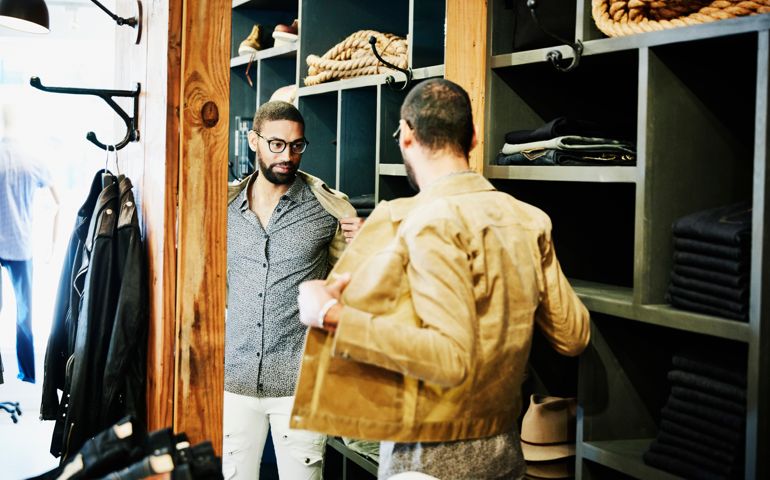 Man trying on jacket while looking in the mirror in mens clothing shop