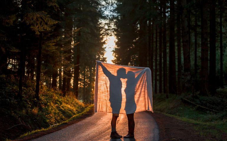 Silhouette of couple holding blanket kissing on country road in forest