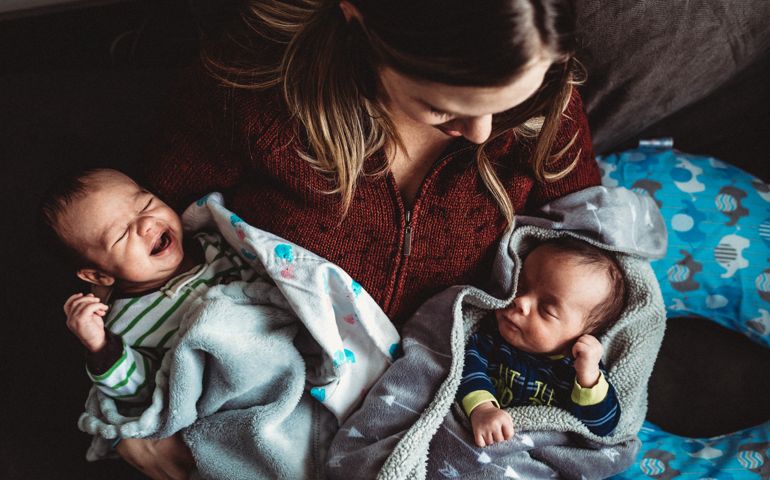 Mother Holds Infant Newborn Twins Together at Home on Lap