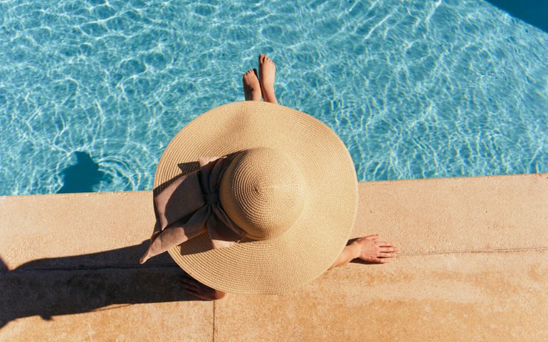 Woman in hat lies near the pool, bright sun