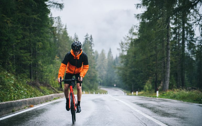 Road bicyclist rides up a wet road in the rain
