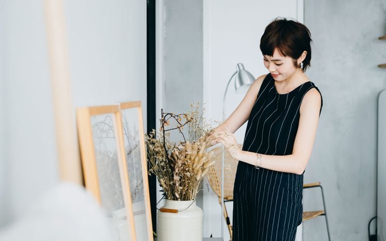 Young Asian woman decorating and arranging a vase with dried plants on cabinet in the living room at home