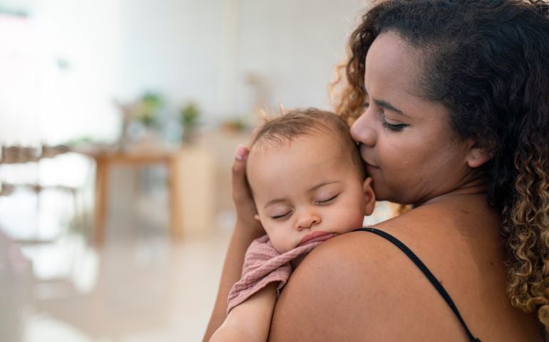 Close Up Of Mother Cuddling Sleeping Baby Daughter At Home