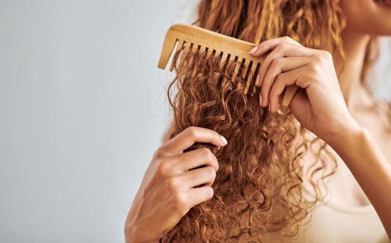 Cleaning, beauty and hair care by woman brush and style her natural, curly hair in bathroom in her home. Hygiene, frizz and damage control with female hands comb natural hair in morning routine