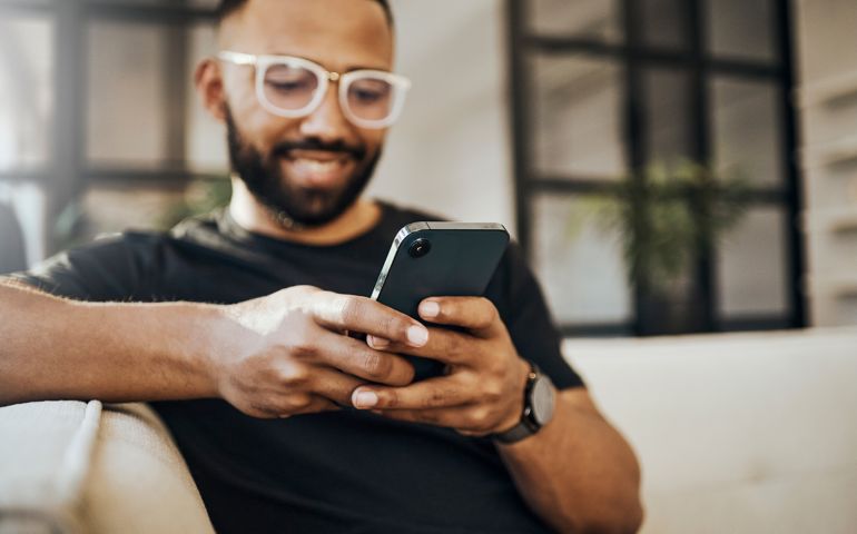 Happy man, social media phone and living room relax, typing smartphone and online communication, reading notification and web on sofa. Smile guy hands, mobile connection and home network technology