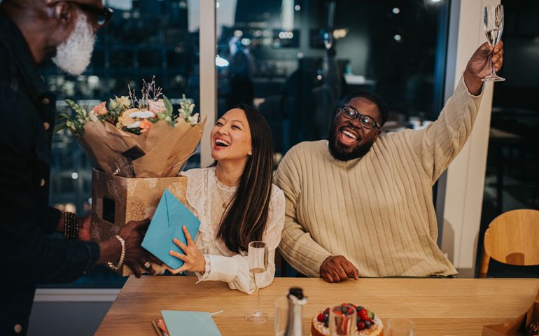 A happy woman is presented with a bouquet of flowers at an after-work office party