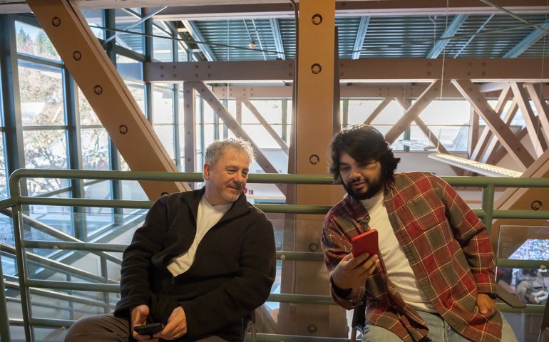 Hispanic Man Showing Senior Man Smartphone Photo in Waiting Area