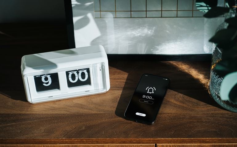 Smartphone on wooden cabinet rings at nine o'clock, next to digital flip clock at home interior. Sunbeam shining through the window on a fresh morning. A brand new day, fresh start, fresh energy, new opportunities. Waking up early for a healthy lifestyle