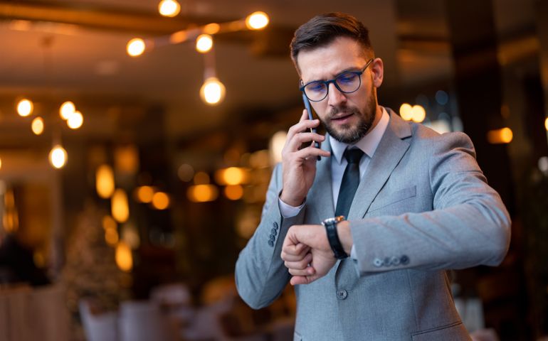 Handsome worried businessman talking on smartphone, looking at hand watch