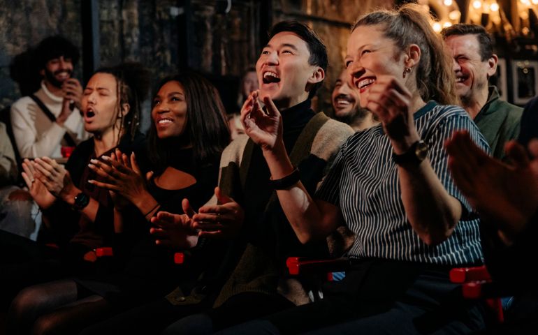 Happy multiracial friends laughing while enjoying comedy show at stage theater
