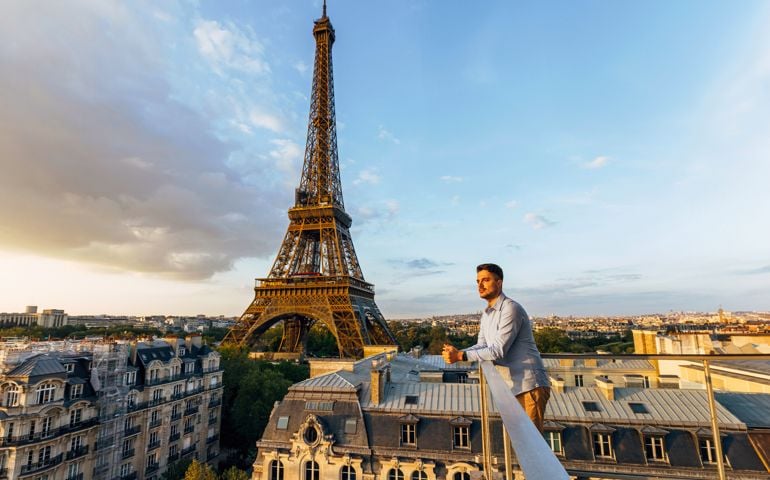 Young man looking at the sunset from the balcony with Eiffel Tower in the background, Paris, France