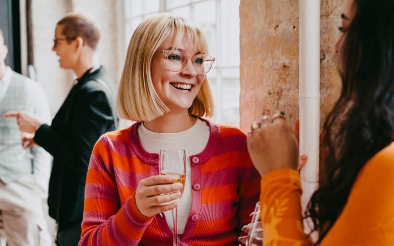 Happy blond businesswoman enjoying drink with female colleague during event at convention center