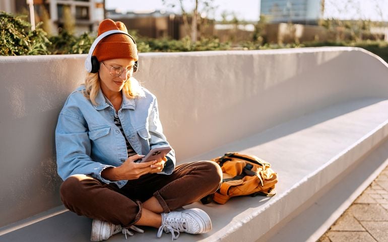 Young hipster woman text messaging while sitting on a bench outdoors