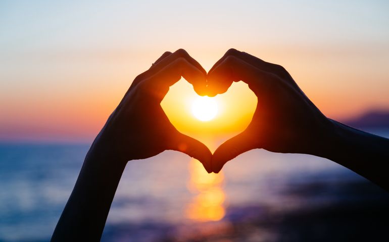hands forming a heart shape with sunset silhouette