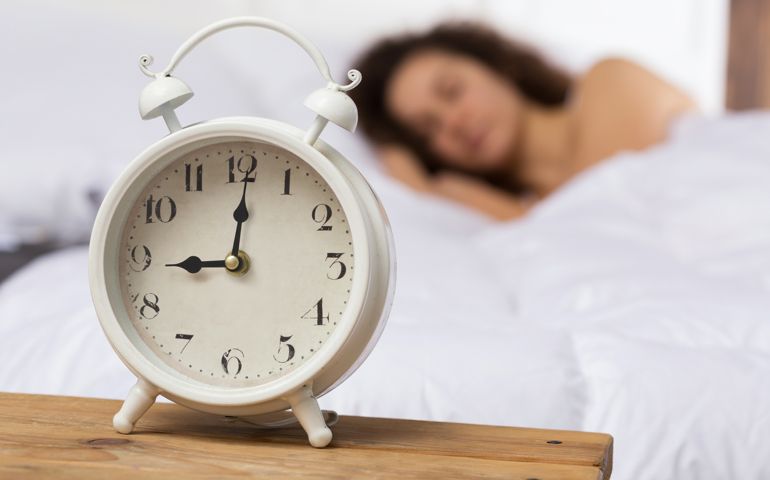 White alarm clock on the background of a sleeping girl.