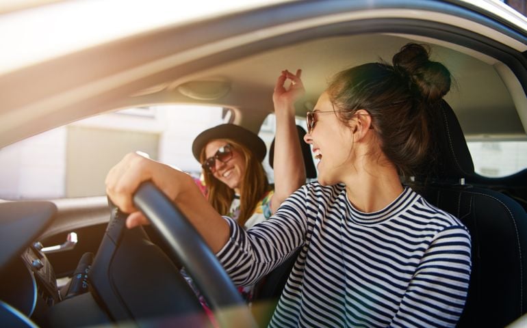 Two young women having fun driving along a street