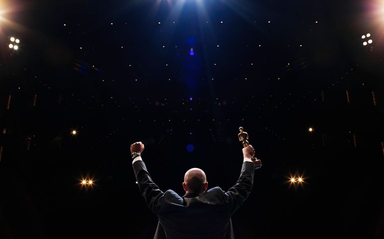 Man holding up award towards audience, rear view