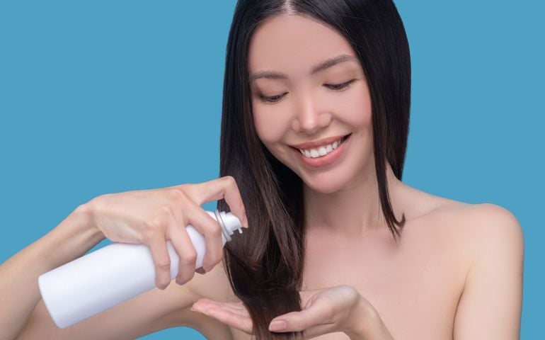 Smiling woman putting hair oi on her hair