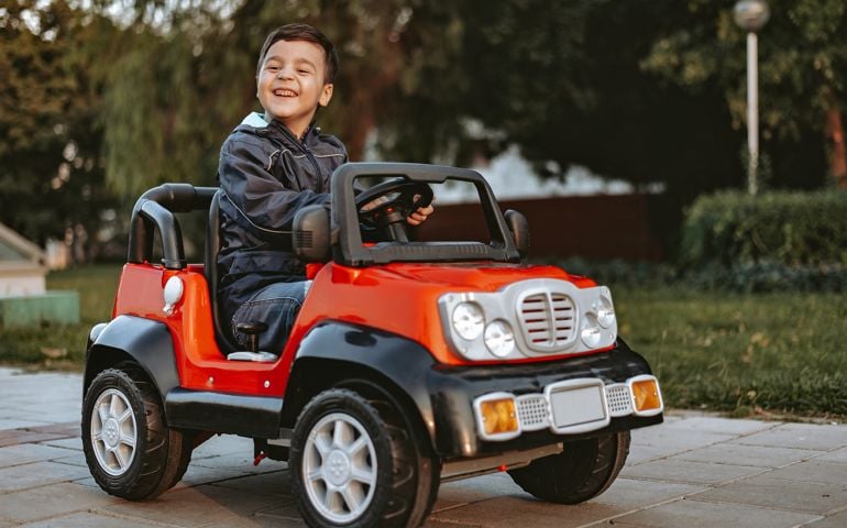 Little boy riding toy car in the garden