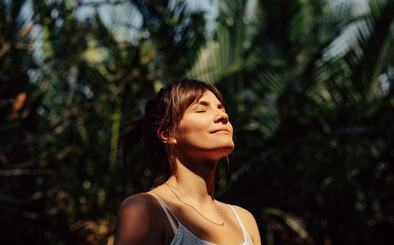 Beautiful Happy Woman Enjoying the Warm Sunlight in a Tropical Public Park