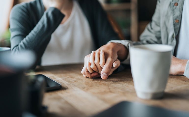 Close up of young Asian couple on a date in cafe, holding hands on coffee table. Two cups of coffee and smartphone on wooden table. Love and care concept