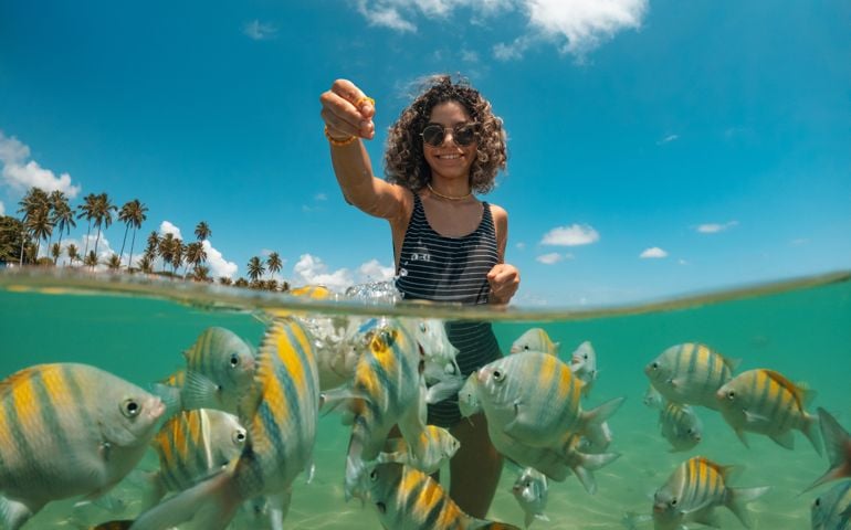 Young woman feeding fish on tropical beach
